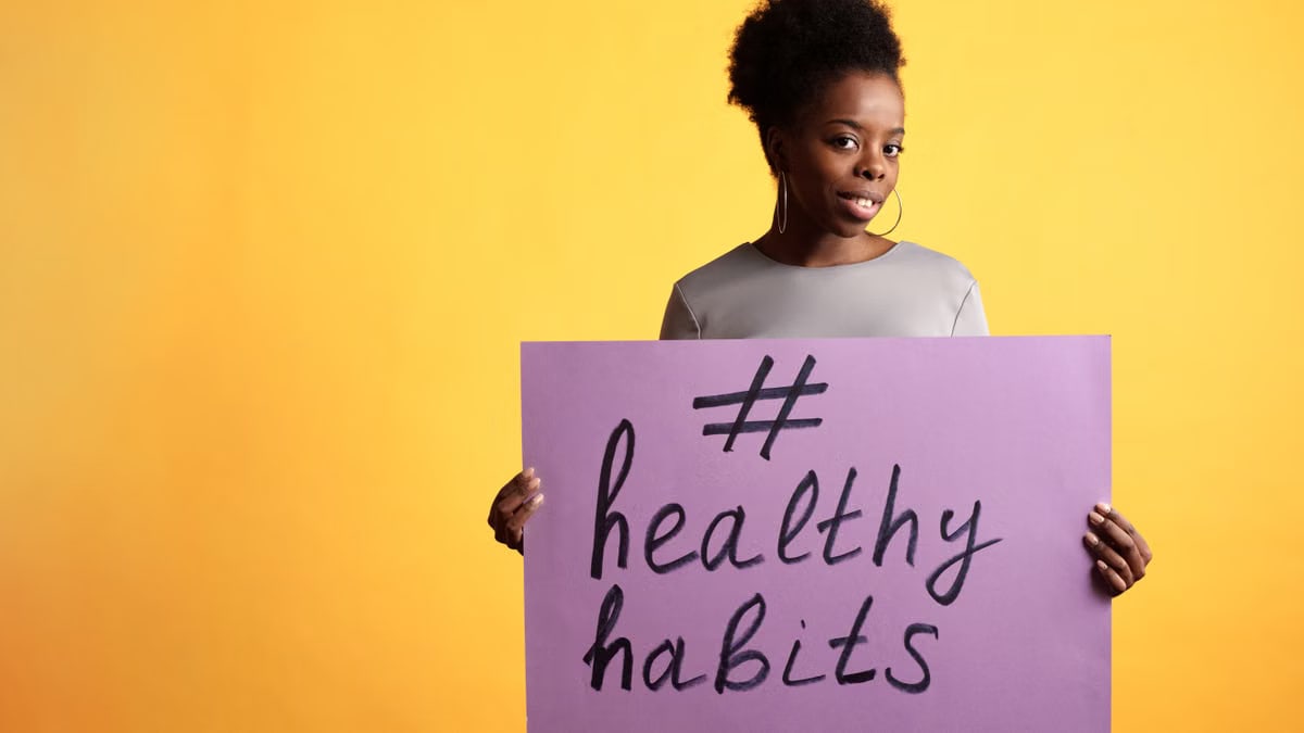 Portrait of a woman holding a healthy habits sign, set against a vibrant yellow background.