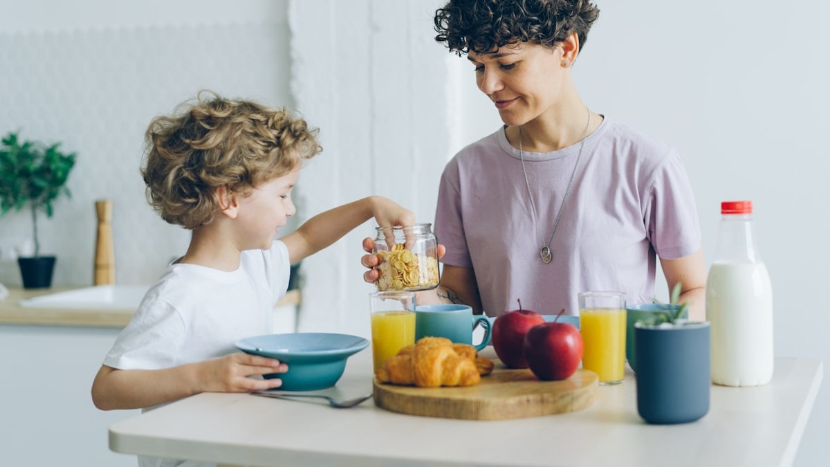 Happy family mother and son eating cereal with milk at home talking